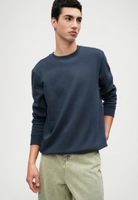 Pullover navy in un tessuto morbido con colletto rotondo e polsini a costine, abbinato a pantaloni in denim verde chiaro. Design minimalista senza motivi.