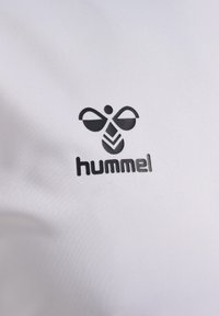 Witte stof met een zwart logo met gestileerde bijelementen en het woord "hummel" in vetgedrukte, duidelijke letters onder het logo.