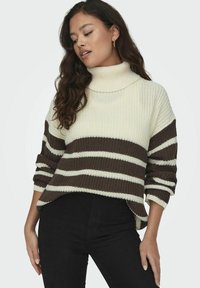 Maglione lavorato a maglia spessa in avorio con strisce orizzontali marroni. Presenta un colletto alto, spalle scese e polsini a coste. Texture morbida.