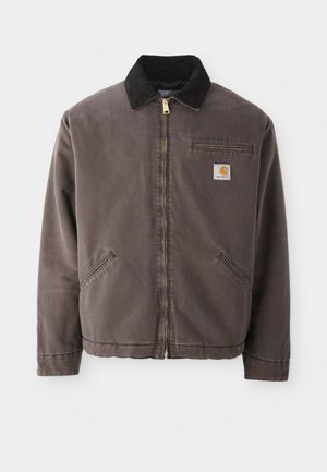 Brown canvas jacket with a black suede collar, gold zipper, side pockets, and a chest pocket featuring a logo patch.