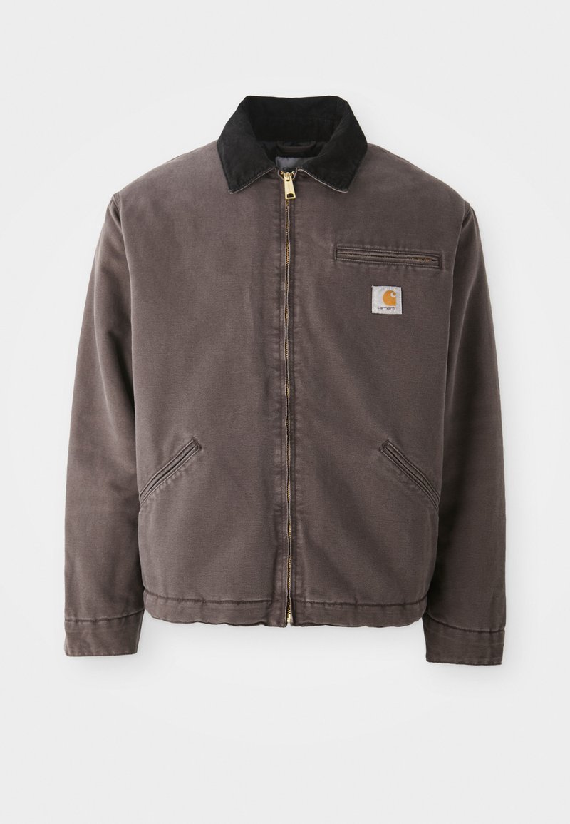 Bruine canvas jas met een zwarte suède kraag, gouden rits, zijzakken en een borstzak met een logo-patch.