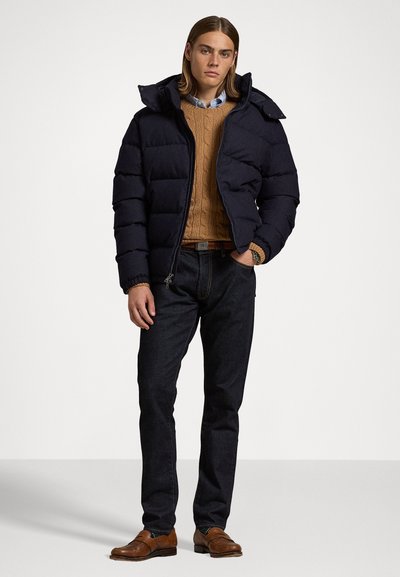 Navy puffer jacket with a hood, cable-knit tan sweater, dark jeans, and brown loafers. Features include ribbed cuffs and a zipper closure.