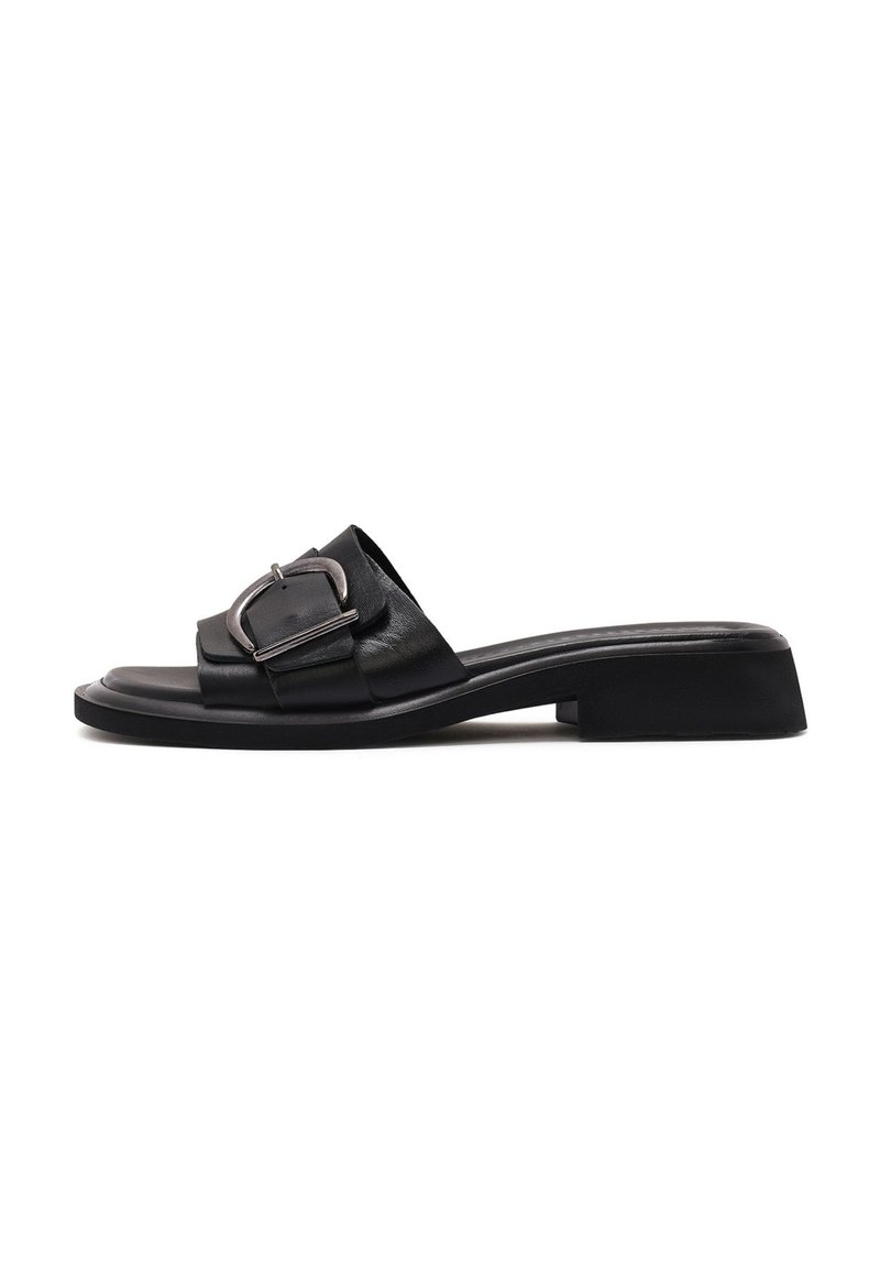 Sandalia de cuero negro deslizable con una correa ancha que presenta una hebilla metálica. Tacón bajo, textura suave y diseño minimalista.