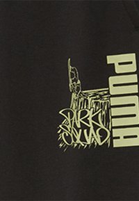 Sudadera negra con un gran logo amarillo "PUMA" y un gráfico estilo graffiti que dice "PARK SQUAD", enfatizando elementos de diseño audaces.