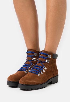 Bottines en daim marron avec des lacets bleus, des œillets en argent et des accents noirs. Présentent une semelle épaisse pour un soutien et une traction.