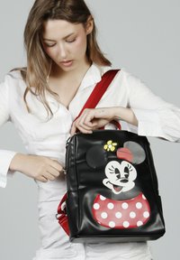 Sac à dos en faux cuir noir avec un grand design de Minnie Mouse, des pois rouges, un accent de fleur jaune et une sangle rouge réglable.