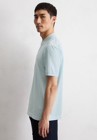 Hellblaues Polohemd aus weichem Stoff, mit klassischem Kragen und kurzen Ärmeln. Auffällige Details sind dezente Farbakzente und ein gerader Saum.