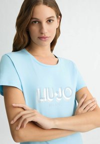 Šviesiai mėlyna trumpomis rankovėmis marškinėliai su blizgia "LIU•JO MILANO"_LOGO. Minkšta medžiaga su apvalia kaklo iškirpte. Paprastas, modernus dizainas.