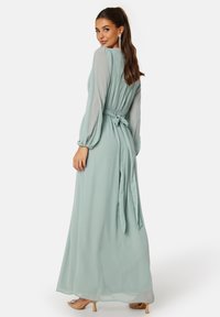 Lange, mintgroene chiffon jurk met lange mouwen, een getailleerde taille en een strikdetail op de rug; gladde textuur en vloeiende vorm.