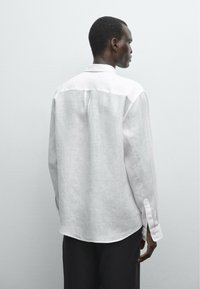 White linen shirt with long sleeves, a straight cut, buttoned cuffs, and a back yoke detail, displayed against a plain background.