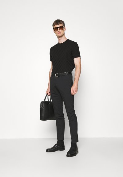 Camisa de manga corta negra texturada, pantalones oscuros de corte slim, cinturón de cuero negro, mocasines, gafas de sol y un bolso negro.