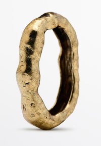 Gestructureerde ring van goudkleurig materiaal; onregelmatige, golvende vorm met een gepolijste buitenkant en matte binnenkant; zichtbare oppervlakte-onregelmatigheden.