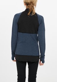 Langærmet top med et blåt teksturdesign og et sort øverste panel, ergonomiske sømme og tommelfingerhuller i ærmerne.