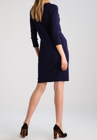 Navy ribbed dress with three-quarter sleeves, knee-length, featuring a back seam and paired with black high heels with tortoiseshell accents.