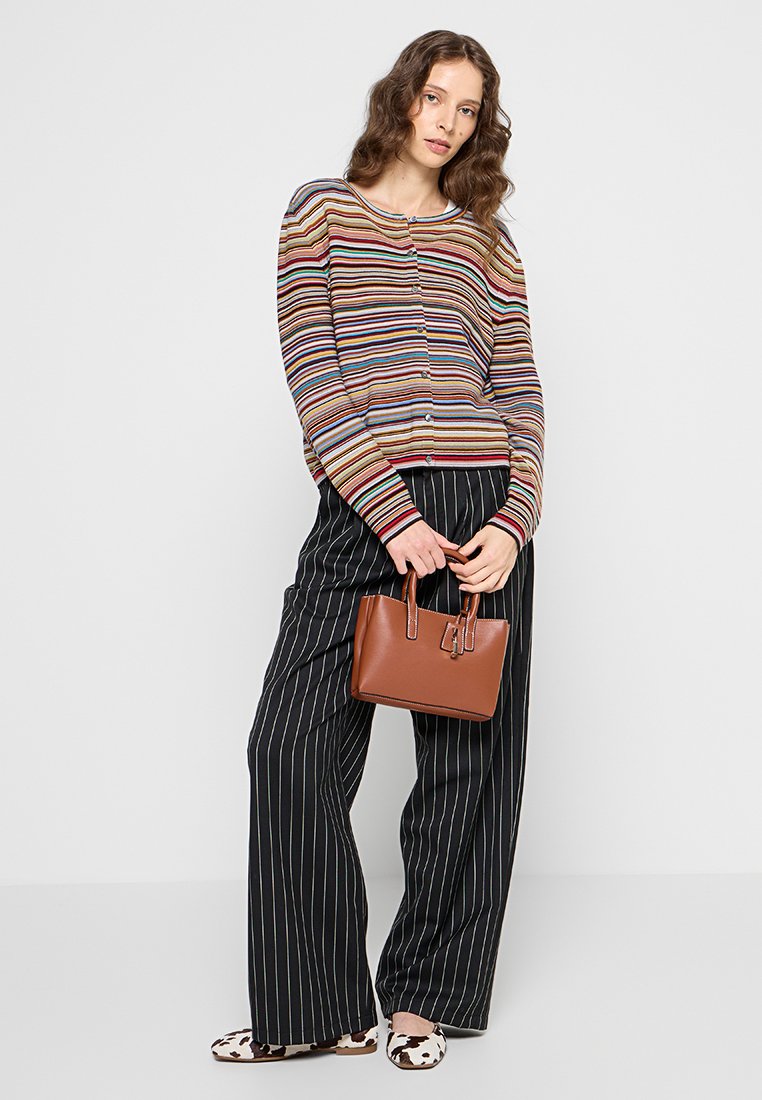 Cardigan rayé multicolore, sac à main en cuir marron, pantalon large à rayures noires et blanches, et chaussures à motif vache. Look décontracté avec des textures.