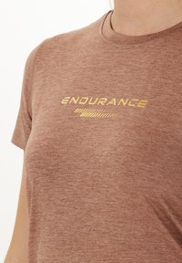 T-shirt marron chiné à manches courtes et encolure ras du cou, avec le texte doré "ENDURANCE" et un design graphique linéaire en dessous.