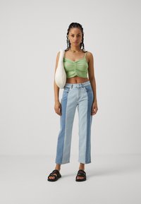 Zeleno nabrana kratka majica, svetlo modri in džins patchwork jeans, črne sandale in krema ramenska torba. Enostaven dizajn z teksturirano tkanino.