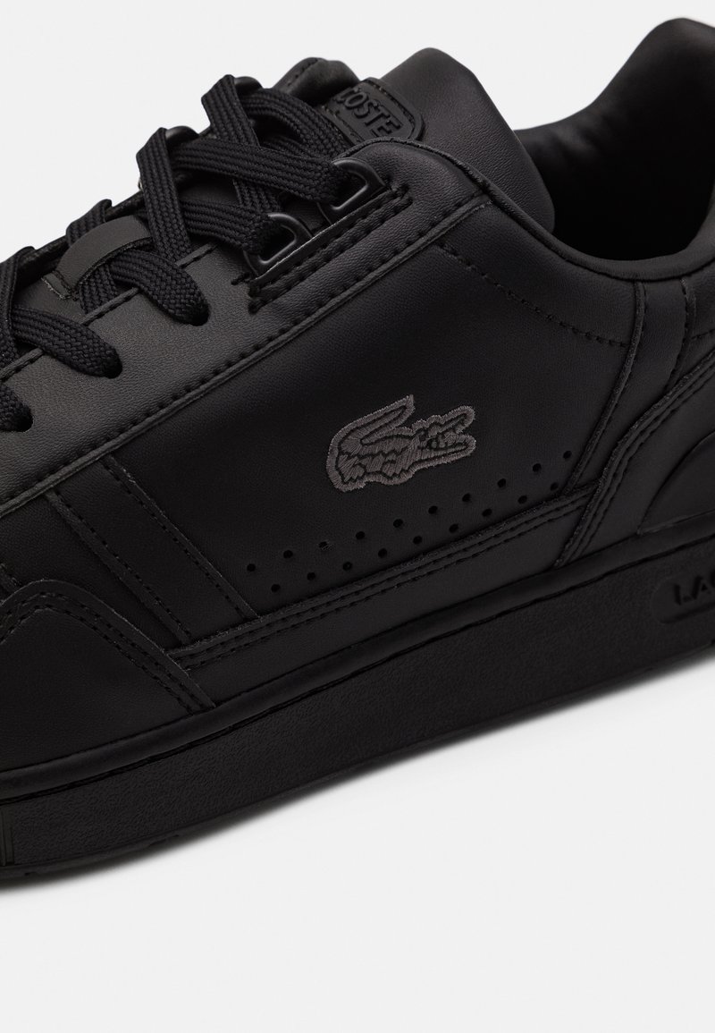 Black leather sneaker featuring a textured surface, rounded toe, perforations, and a tonal embroidered logo. Flat black laces and rubber sole.