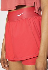 Röda idrottsshorts med en bred elastisk midjeband som har en vit Nike-logotyp. Tillverkade av lätt, andningsbart material med en lagerdesign.