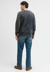 Donkergrijze sweatshirt met vervaagde textuur, ronde hals, en zichtbare stiksels, gecombineerd met blauwe jeans en bruine instappers.