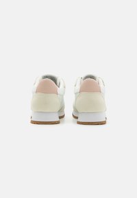 Hvite sneakers med en lys rosa bakpanel, semsket detaljer og en teksturert gummisåle. Enkelt design med polstret hælholder.