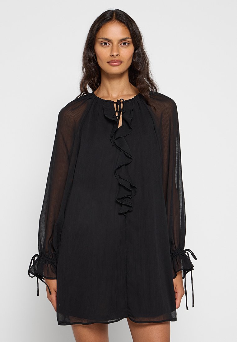 Robe noire en tissu transparent, dotée de manches longues avec des fermetures à lien et d'un design à volants sur le devant, taillée dans une silhouette décontractée.