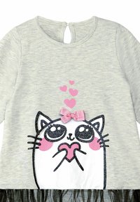 Grijze langemouwen shirt met een kattenafbeelding met grote ogen, roze harten en een roze strik. De onderkant heeft een zwarte tule-accent.