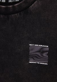 Schwarzes T-Shirt aus strukturiertem Stoff, runder Ausschnitt und einem Frontgraphic in Lila und Weiß, das die Marke und den Slogan in moderner Schrift zeigt.