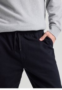 Navy pants with a relaxed fit, made of soft fabric. Features elastic waistband with drawstring and side pockets. Paired with a gray sweatshirt.