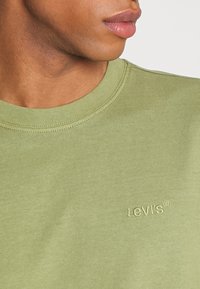 Sweat-shirt en coton vert avec un col rond et un tissu légèrement texturé. Présente un logo "Levi's" brodé en vert assorti sur la poitrine.