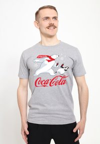 T-shirt di cotone grigio con una grafica di un orso polare e un pinguino con i loghi della Coca-Cola in rosso. Design a maniche corte e scollo rotondo.