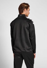 Sort atletisk jakke med høj krave, lange �ærmer og hvide side-striber. Glat tekstur med logo detaljer på ryggen.