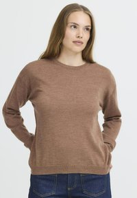 Brązowy sweter dzianinowy z okrągłym dekoltem, długimi rękawami i luźnym krojem. Miękka tekstura z prążkowanymi mankietami i dołem, w zestawie z ciemnoniebieskimi dżinsami.