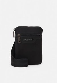 Bolso negro de nylon para llevar cruzado, con cierre superior y bolsillo delantero con cremallera. Presenta detalle de logotipo y una correa de hombro tejida. Textura suave, diseño minimalista.