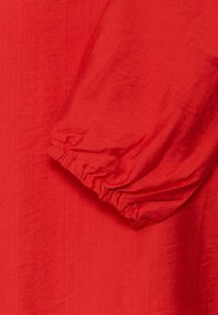 Gros plan d'une longue manche en tissu rouge avec un poignet élastique froncé et une texture de tissage visible.