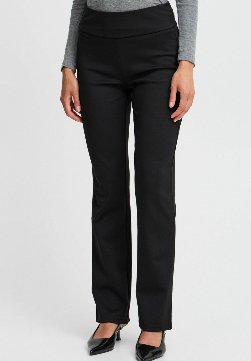 Black, stretchy pants with a high waistband. Designed with a straight leg, smooth texture, and subtle sheen, paired with black heels.