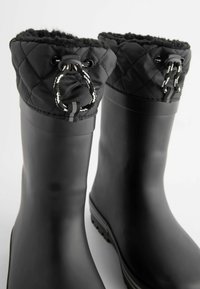 Bottes noires imperméables avec un col en nylon matelassé, dotées d'un système de fermeture par cordon, de semelles en caoutchouc texturé et d'une texture de corps lisse.