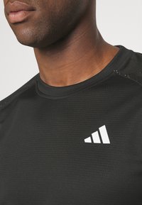 Camiseta atlética negra con una superficie texturada. Presenta un logo triangular blanco en la parte izquierda del pecho y un diseño de cuello redondo.