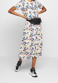Robe blanche ornée d'un imprimé géométrique coloré, associée à une ceinture noire et des chaussures de sport noir et blanc.
