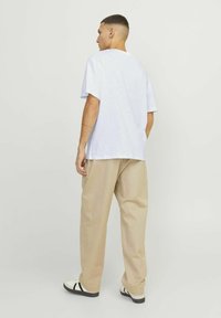 Hvid kortærmet t-shirt med en afslappet pasform, parret med beige vidde bukser og hvide sneakers med sorte striber. Enkel baggrund.