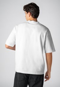 Weißes Baumwoll-T-Shirt mit kurzen Ärmeln, lockerer Passform, Rundhalsausschnitt und glatter Textur. Die Ansicht zeigt die Rückseite ohne sichtbare Grafiken oder Logos.