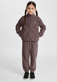 Fleecejacka och byxor i mörk lila, med hög krage, dragkedjestängning och en broderad logga på jackan. Byxorna har elastiska muddar.