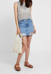Top sin mangas con estampado floral, minifalda de mezclilla con desgastes, sandalias de plataforma color marrón y bolso de macramé color crema con asas de bambú.