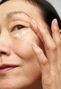Cream applied to the under-eye area with a light-colored, smooth texture. Skin appears soft with slight natural blemishes.
