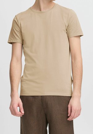 Beige kortærmet t-shirt lavet af letvægtsbomuld. Rund halsudskæring med glat tekstur, parret med brune teksturerede bukser.