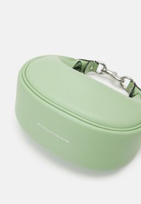 Sac à main en cuir vert clair avec bords arrondis et anse chaîne argentée, affichant l’étiquette « Cuir véritable tanné au gant ».