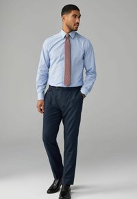 Camisa de vestir a rayas azul claro, corbata geométrica roja, pantalones azul marino oscuros y zapatos negros. Presenta un cuello clásico y acentos de botones.