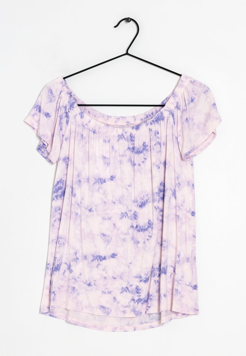 Blouse manches courtes tie-dye violet clair et blanc avec encolure froncée suspendue à un cintre noir sur fond blanc.