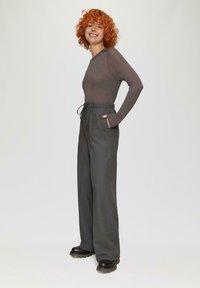 Dunkelgraue weitem Hosen mit Kordelzugbund und Taschen, kombiniert mit einem eng anliegenden, glitzernden braunen Langarmoberteil. Schwarze Stiefel mit dickem Sohlen.