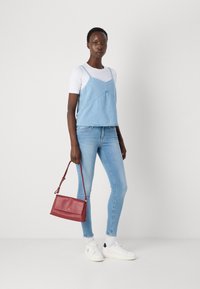 Light blue denim crop top with spaghetti straps over a white t-shirt, paired with light blue skinny jeans and a red handbag. White sneakers.